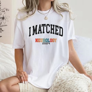 May include: White t-shirt with black text that reads "I MATCHED NEUROLOGY 2024". The word "NEUROLOGY" is in rainbow colours.
