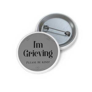 Op de afbeelding: Een grijze knop met een witte rand en de tekst "I'm Grieving Please Be Kind!" in zwart.