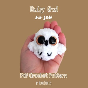 May include: A small, white, fuzzy crochet baby owl toy with large, round, black eyes featuring copper-coloured rims and a small black beak. The text reads Baby Owl no sew Pdf Crochet Pattern by HOOKSTORIES.