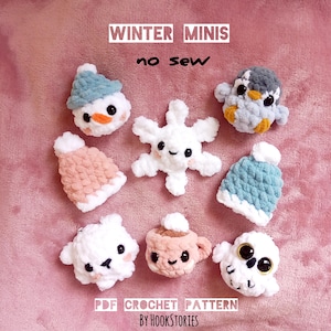 May include: A selection of handmade crochet winter-themed mini figures, including a snowman, penguin, snowflake, bear, owl, and a cup of cocoa. The figures are in shades of white, blue, pink, and orange. Text on the image reads "Winter Minis" and "no sew".