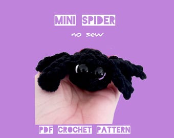 Op de afbeelding: Een zwarte gehaakte spin met grote, glanzende zwarte ogen en een rode accent. De tekst "MINI SPIDER no sew" staat boven de spin en "PDF CROCHET PATTERN BY HOOKSTORIES" eronder, alles op een paarse achtergrond.