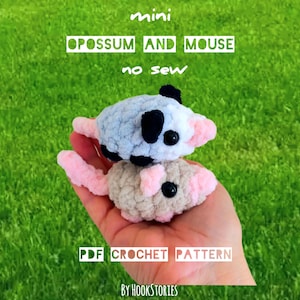 May include: Two mini crochet animals, an opossum and a mouse, are stacked on top of each other. The opossum is light blue with black spots and a pink tail. The mouse is tan with a pink nose and tail. The text reads "mini opossum and mouse no sew PDF crochet pattern".