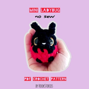 Puede incluir: Un juguete de mariquita de ganchillo hecho a mano en negro y rojo, sostenido en una mano. La mariquita tiene ojos grandes con borde dorado y pequeñas antenas. El texto en la imagen dice "MINI LADYBUG no sew" y "PDF CROCHET PATTERN BY HOOKSTORIES."