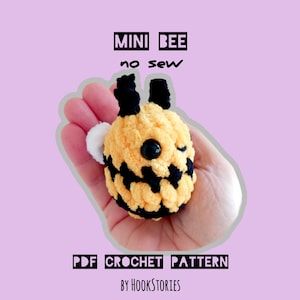 May include: A crocheted mini bee with yellow and black stripes, black eyes, and black antennae. The bee is held in a hand. Text on the image reads "MINI BEE no sew" and "PDF CROCHET PATTERN BY HOOKSTORIES."