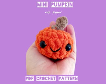 Może przedstawiać: Mała, pomarańczowa szydełkowa dynia z uśmiechniętą twarzą i brązową łodygą trzymana jest w dłoni. Tekst "MINI PUMPKIN no sew" i "PDF CROCHET PATTERN BY HOOKSTORIES" jest wyświetlany na fioletowym tle.