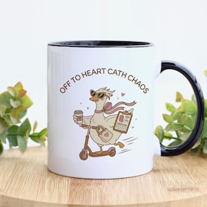 May include: A white ceramic mug with a black rim and handle featuring a cartoon goose wearing sunglasses, riding a scooter, and holding a coffee cup and a clipboard. The text "OFF TO HEART CATH CHAOS" is printed in brown above the goose illustration.