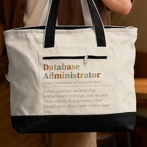 May include: A cream-colored canvas tote bag with black handles and a black base. The front features a zippered pocket and printed text that reads: Database Administrator noun [deɪtəbeɪs ədˈmɪnɪstreɪtər] A data guardian maintaining performance, backups, and security.
