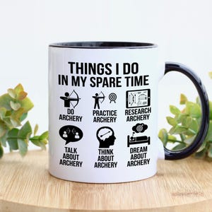 May include: White ceramic mug with a black interior and handle. The mug features the text "THINGS I DO IN MY SPARE TIME" with illustrations and text about archery, including "DO ARCHERY", "PRACTICE ARCHERY", and "DREAM ABOUT ARCHERY".