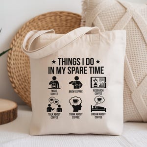 May include: Cream-colored tote bag with the text "THINGS I DO IN MY SPARE TIME" and illustrations about coffee. The illustrations include making, brewing, and researching coffee, as well as talking, thinking, and dreaming about coffee.
