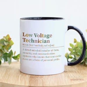 May include: A white ceramic mug with a black handle and rim, featuring the printed text: Low Voltage Technician, noun, a detail-minded installer of data, security, and communication systems who knows that neat cable runs are a form of personal pride.