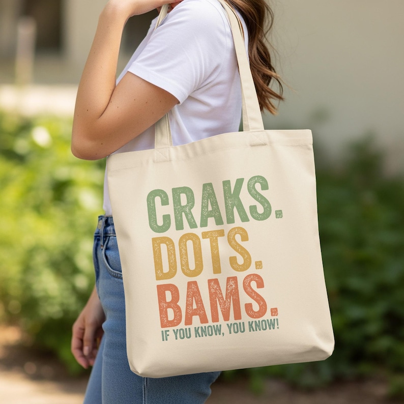 Cream tote bag with "Craks. Dots. Bams. If you know, you know!" text.