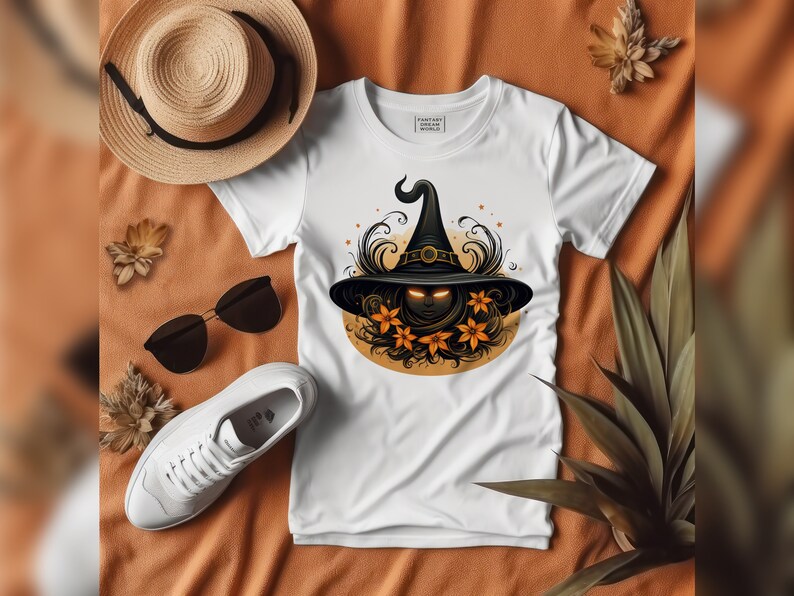 May include: White t-shirt featuring a Halloween-themed graphic of a witch's hat with glowing eyes, surrounded by orange flowers and decorative swirls. The shirt is displayed with a straw hat, sunglasses, and white sneakers on an orange surface.