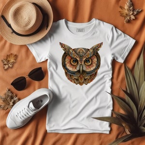 May include: White t-shirt with a colorful, detailed owl graphic on the front. The owl has large, round eyes and intricate patterns throughout its feathers. The text "Fantasy World" is printed above the owl.