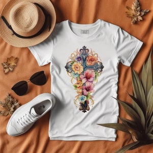 May include: White t-shirt with a floral cross design. The cross is made of dark gray metal and is surrounded by pink, purple, and yellow flowers. The shirt has the text "Fantasy Art World" printed on the front.