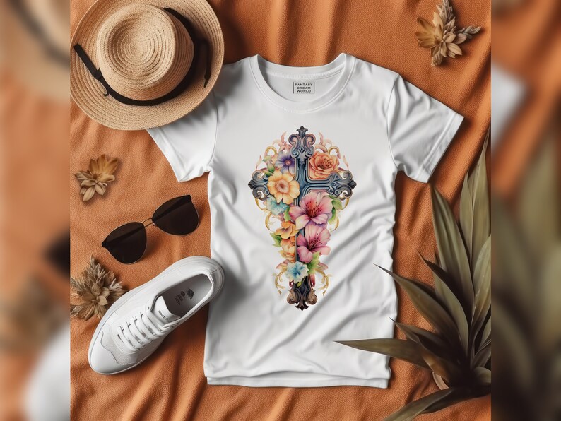 May include: White t-shirt with a floral cross design. The cross is made of dark gray metal and is surrounded by pink, purple, and yellow flowers. The shirt has the text "Fantasy Art World" printed on the front.