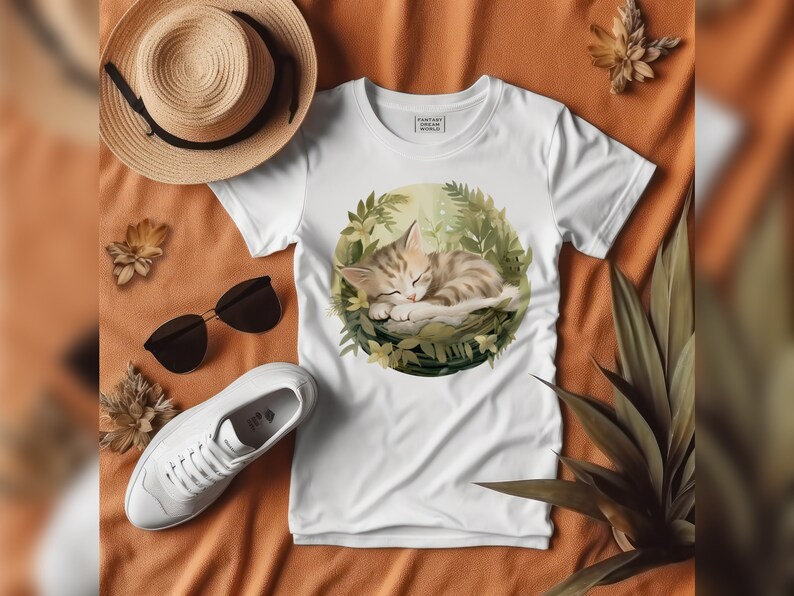 Puede incluir: Camiseta blanca con un gr&aacute;fico de un gato durmiendo en un entorno verde y frondoso. El texto "Fantasy World" est&aacute; impreso en la camiseta.