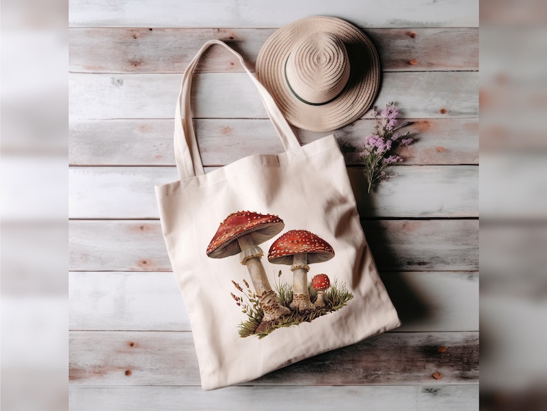 May include: A white canvas tote bag with a design of three red and white mushrooms on a green background. The bag has two long straps and is lying on a wooden surface.