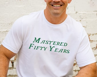 Peut inclure: T-shirt blanc avec un texte vert qui dit "Mastered Fifty Years".