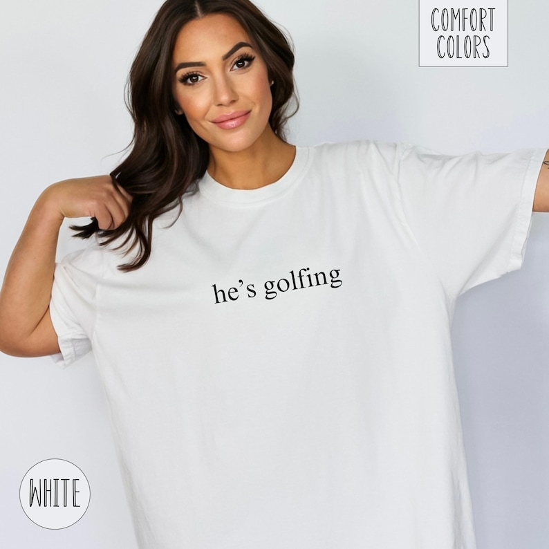 May include: White t-shirt with the text "he's golfing" printed in black.