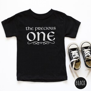May include: Black short-sleeved t-shirt with white text that reads "the precious one" in a decorative font.