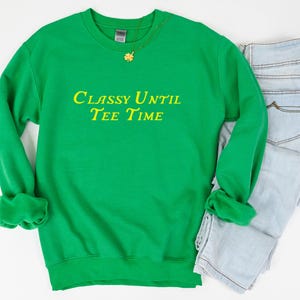 以下が含まれることがあります： 黄色の文字で「Classy Until Tee Time」と書かれた緑色のスウェットシャツです。