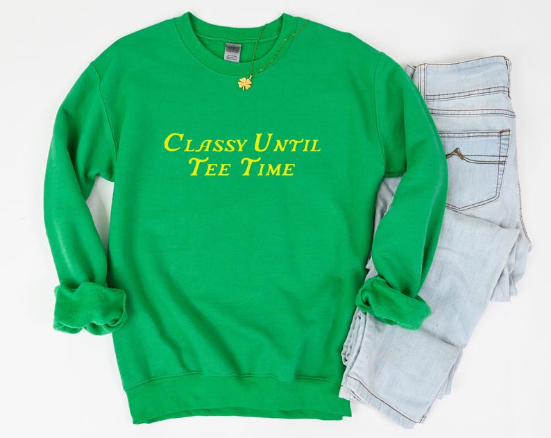 以下が含まれることがあります： 黄色の文字で「Classy Until Tee Time」と書かれた緑色のスウェットシャツです。