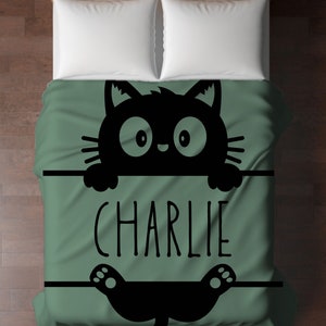 May include: A green and black bedding set with a cartoon black cat peeking over the top and the name "CHARLIE" printed on the front.