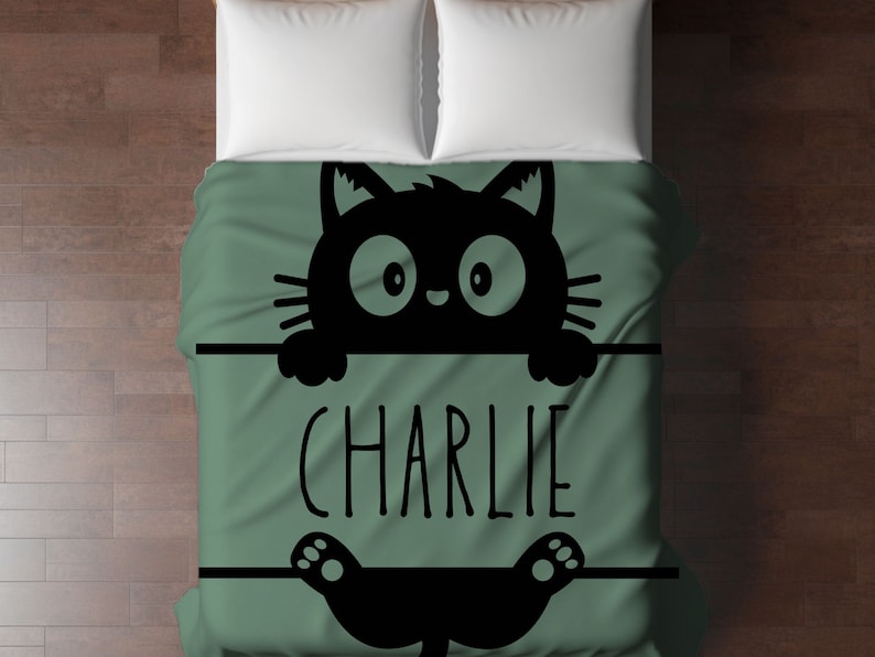 May include: A green and black bedding set with a cartoon black cat peeking over the top and the name "CHARLIE" printed on the front.