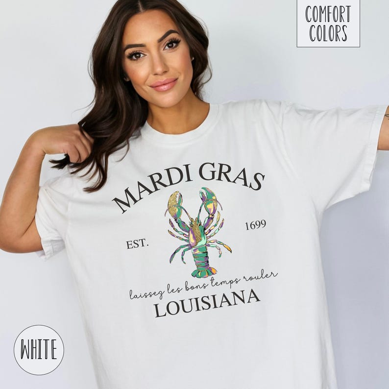 May include: White t-shirt with a Mardi Gras design featuring a colorful lobster, the text "Mardi Gras", "Est. 1699", "Laissez les bons temps rouler", and "Louisiana".