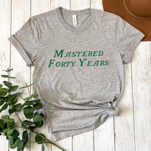 May include: A grey t-shirt with the text "Mastered Forty Years" printed in green.