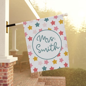May include: A white flag with a colorful star pattern and the text "Mrs. Smith" in a circle. The flag is hanging from a pole.