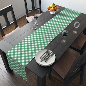 May include: A green and white checkered table runner on a dark wood table with two wine glasses and a plate of silverware.