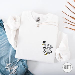 May include: White sweatshirt with a black and white embroidered goose wearing a top hat and bow tie. The text "Mr. Silly Goose" is embroidered below the goose.