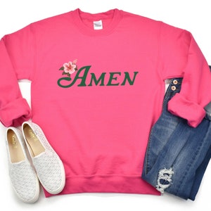 May include: Pink sweatshirt with a green floral design and the word "AMEN" in green lettering.