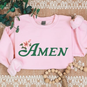 May include: Pink sweatshirt with a green "AMEN" graphic and a pink flower design.