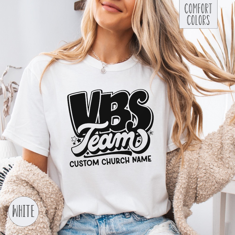 Op de afbeelding: Wit T-shirt met een zwart-witte afbeelding met de tekst "VBS Team" en "Custom Church Name".