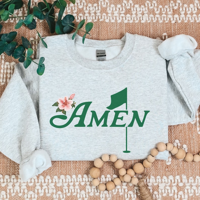 May include: A gray sweatshirt with a green golf flag and the word "AMEN" in green lettering. A pink flower is next to the word "AMEN".