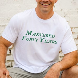 May include: White t-shirt with green text that reads "Mastered Forty Years".