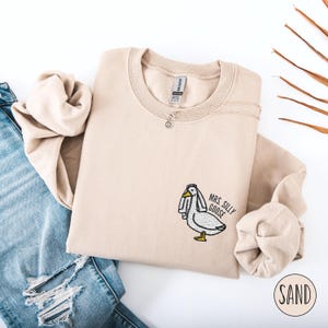 May include: A beige sweatshirt with an embroidered image of a goose wearing a veil and the text "Mrs. Silly Goose".