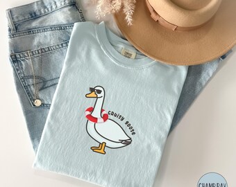 May include: A light blue t-shirt with a cartoon illustration of a goose wearing sunglasses and a life preserver. The text "Cruisy Goose" is written below the goose.