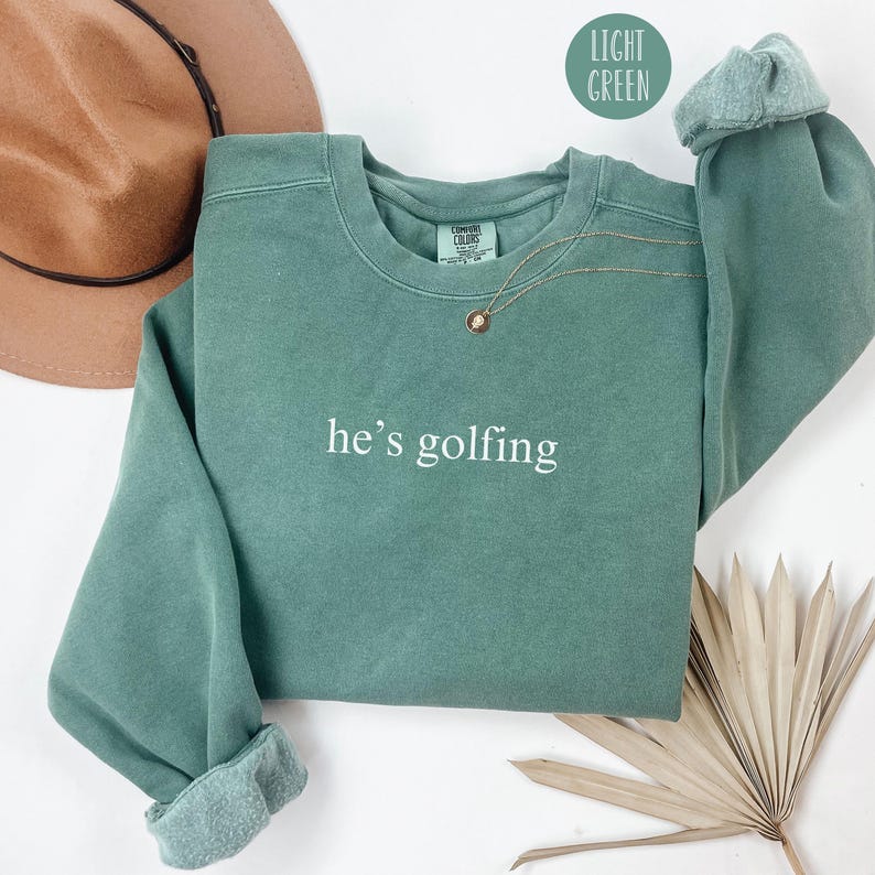 May include: A light green sweatshirt with the text "he's golfing" in white lettering.