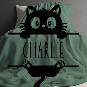 May include: A green blanket with a black cat silhouette peeking over the top. The cat is holding a sign that says "CHARLIE".