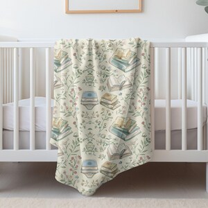 May include: A white crib with a cream and green baby blanket featuring a pattern of stacked books and floral sprigs.