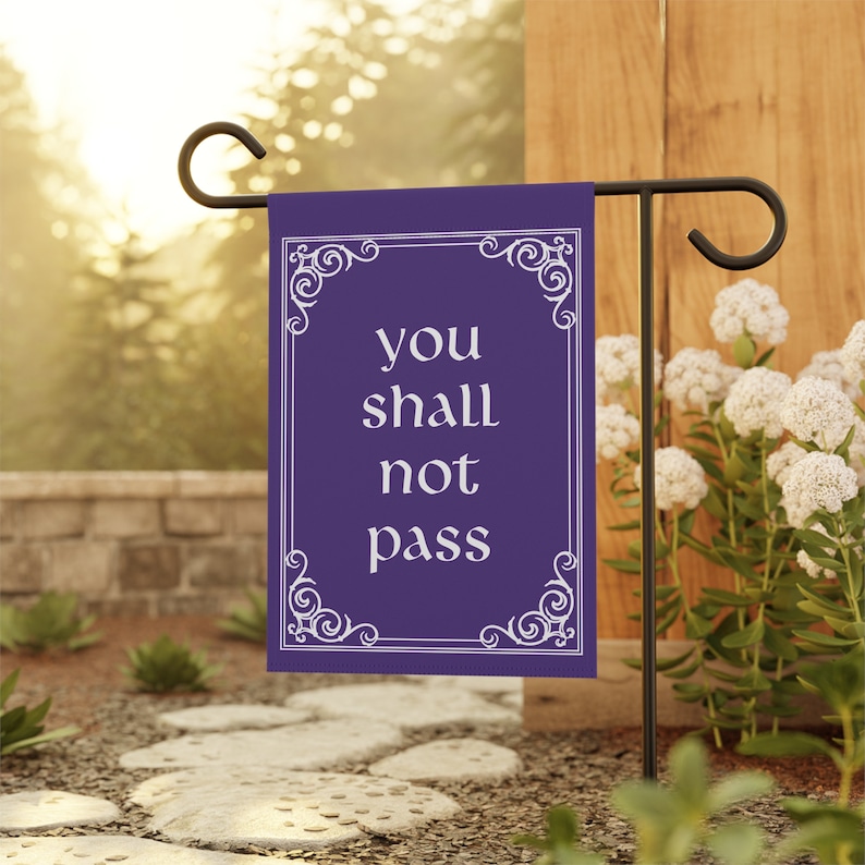 May include: Purple garden flag with a white ornate frame and the text "you shall not pass" in white.