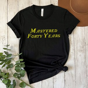 May include: Black t-shirt with the text "Mastered Forty Years" in yellow lettering.
