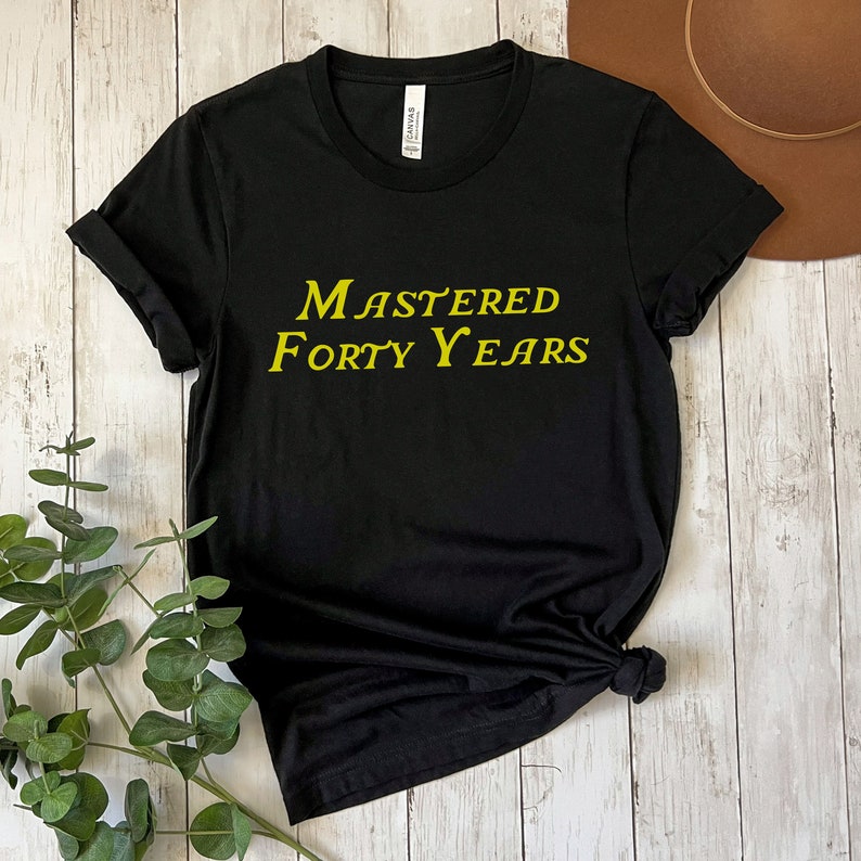 May include: Black t-shirt with the text "Mastered Forty Years" in yellow lettering.