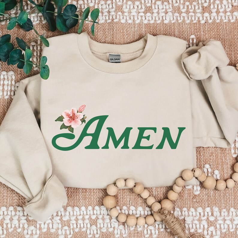 May include: A beige sweatshirt with the word "AMEN" in green cursive lettering and a pink flower graphic.