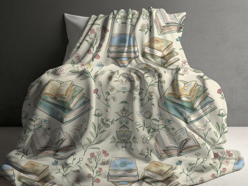 May include: A cream-colored throw blanket with a floral pattern featuring green leaves and pink, blue, and yellow flowers. The blanket has a repeating pattern of stacks of books with open pages.