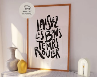 May include: A black and white art print featuring the French phrase "Laissez les bons temps rouler" in a stylised font. The print is framed in a light wood frame and is displayed on a white dresser with a white tiled top.