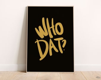 May include: A framed art print with the words "WHO DAT?" in gold brush lettering on a black background. The artwork is displayed against a white wall and a wooden floor.